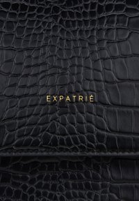 Schwarze Lederhandtasche mit Krokodilprägung, ausgestattet mit einem goldenen "EXPATRIÉ"-Logo. Glatte Oberfläche mit sauberen Nahtdetails.