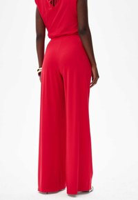 Wide-leg jumpsuit in bright red fabric. Sleeveless design with a back keyhole detail. Smooth texture and flowing silhouette.