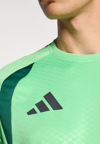 Green athletic shirt with black accents, featuring a textured pattern and a prominent black Adidas logo on the front.