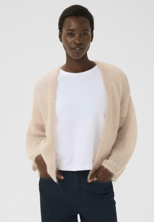 Helle rosa flauschige Strickjacke aus Mischmohair, mit offener Vorderseite, langen Ärmeln, getragen über einem weißen T-Shirt, kombiniert mit dunklen Jeans.