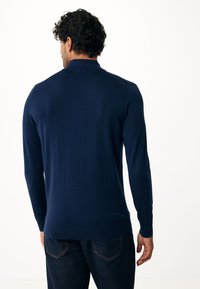 Camisa de manga larga azul marino en material de punto suave con cuello y un diseño ajustado, combinada con jeans de mezclilla oscuros. Textura suave, detalles mínimos.