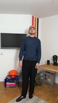 Μπλε ναυτικό φούτερ με ριμπ τελείωμα και μανσέτες, μαύρο παντελόνι και καφέ παπούτσια. Αξεσουάρ περιλαμβάνουν ένα μποέζ καπέλο και ένα ρολόι στον καρπό.