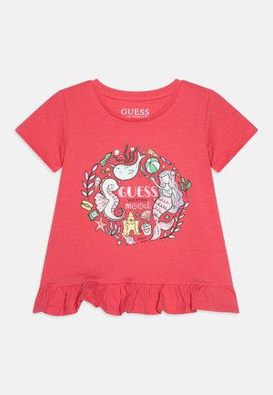 Camiseta coral de manga corta para niño pequeño con bajo con volante, ilustraciones con tema costero y texto "GUESS Vacation Mood" en un diseño circular central.
