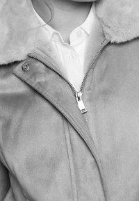 Chaqueta gris de ante con cuello de piel sintética, cremallera plateada y cierre de presión. Presenta una textura suave y un brillo sutil.