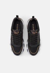 Sneaker nere realizzate con materiali in rete e pelle; presentano dettagli dorati, una spessa suola bianca e il marchio "GUESS" sulla soletta nera.