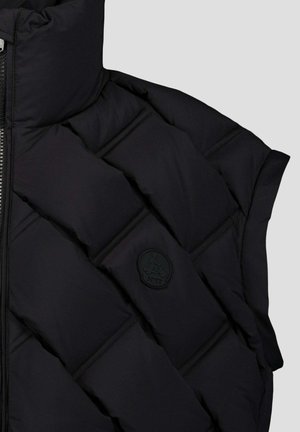 Zwarte gewatteerde jas mouw met horizontale stiksels en een zwart rond JOTT-logo patch, weergegeven tegen een lichtgrijze achtergrond.