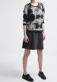 Svart och vit mönstrad sweatshirt med långa ärmar och rundad halsringning, kombinerad med en grå kjol och svarta snörskor.