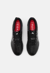 Zapatillas de fútbol de cuero negro con una textura suave, que cuentan con plantillas rojas, cordones negros y acentos blancos a lo largo de los lados.