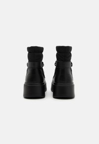 Black ankle boots featuring a smooth leather exterior, padded collar, and a chunky platform sole. Minimalist design with subtle stitching details.
