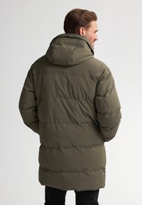 Parka rembourrée en vert olive, dotée d'une capuche, d'une longueur longue, d'une finition texturée et de coutures horizontales pour l'isolation et la chaleur.