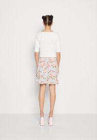 Crop top blanc côtelé à manches courtes associé à une jupe à volants bleu clair à motifs floraux. Le mannequin porte des chaussures roses à talons blocs.