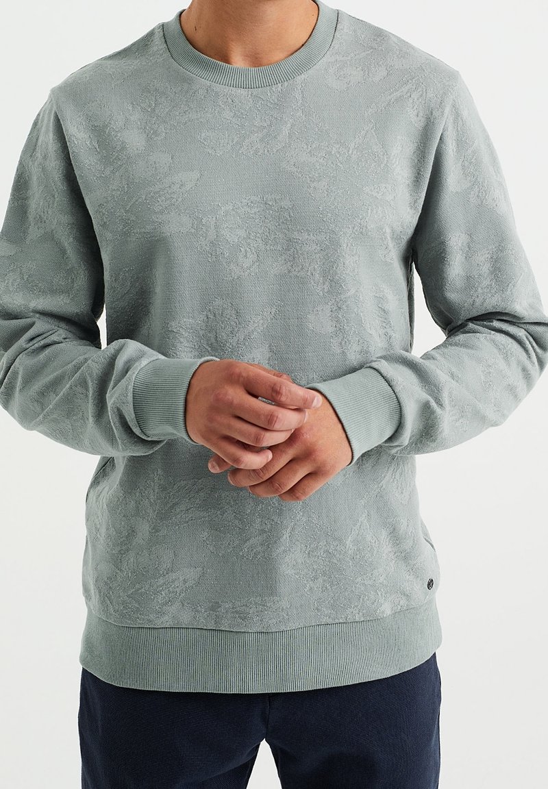 Ljusgrön sweatshirt med en texturerad blommönster, ribbade muddar och fåll, rund halsringning och mjukt tyg.