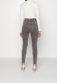 Šedé vysoké skinny džíny s vybledlým vzorem, dvěma zadními kapsami a logem CK na pase, doplněné bílým topem s dlouhým rukávem.