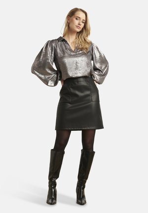 Metaalzilverblouse met pofmouwen, gecombineerd met een zwarte leren minirok. Lange zwarte glanzende laarzen maken de look af.