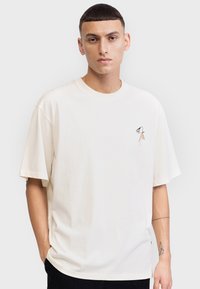 Roomkleurig oversized T-shirt met korte mouwen, voorzien van een kleine bloemrijke borduring in zwart en oranje op de linkerborst.