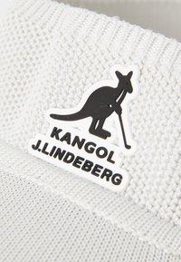 Hvid strikket hat med en tekstureret overflade. Har et sort-hvidt logo, der viser en kænguru med en golfkølle.