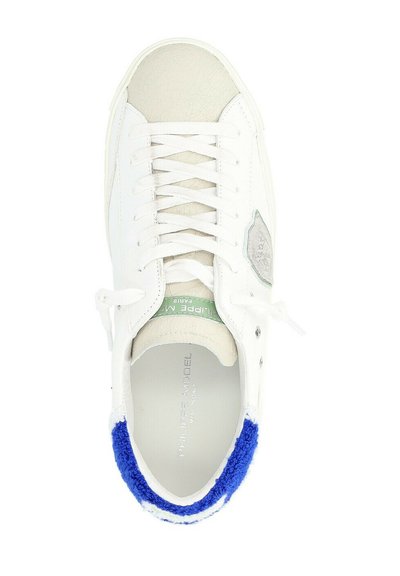 Sneaker bianco in pelle con punta testurizzata, lacci piatti, accenti verdi e blu, e un bordo in spugna blu attorno alla caviglia. Dettaglio del logo argentato all'interno.
