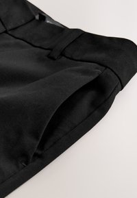 Zwarte stoffen shorts met een gladde textuur, voorzien van een tailleband, zijzak en nette stiksels langs de randen.