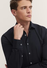 Dunkelblaues Hemd mit klassischem Kragen, sichtbarknöpfen und langen Ärmeln. Glatte Stoffstruktur, minimalistische Gestaltung.