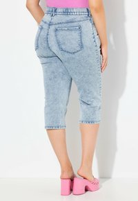 Vaaleansiniset denim-capri-housut, joissa on korkeampi vyötärö, takataskut ja käänteet, yhdistettynä vaaleanpunaisiin korollisiin muloihin.