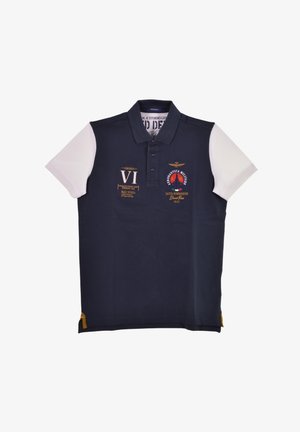 Polo di colore blu navy con maniche corte bianche, dotato di vari patch ricamati e un piccolo accento giallo all'orlo.