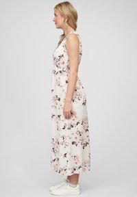 Floral maxi-jurk in crème met roze en bruine bloemen, mouwloos, met een getailleerde taille en een vloeiende rok. Draag het met witte sneakers.