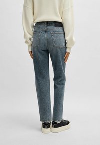 Jeans de tiro alto de color azul claro con pierna recta, dobladillo deshilachado y dos bolsillos traseros, combinados con zapatillas negras y un suéter color crema.