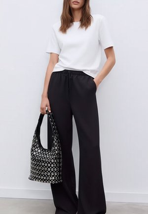 Camiseta blanca de manga corta combinada con pantalones anchos de tiro alto negros, sosteniendo un bolso negro con adornos circulares plateados.