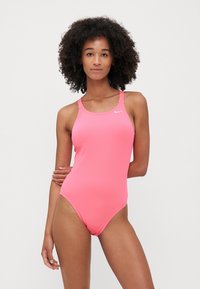 Costume intero di colore rosa brillante realizzato in tessuto liscio, con scollatura rotonda e design a schiena scoperta. Logo Nike sul petto.