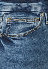 Jeans i denim med en ljusblå tvätt, med synlig sömnad i orange. Inkluderar en framficka och en metallknappslutning.