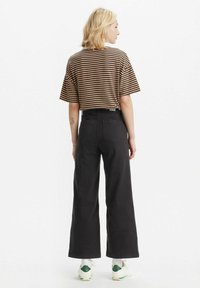 Gestreept bruin en beige crop-top gecombineerd met hoge zwarte wijde broek en sneakers met groene accenten.