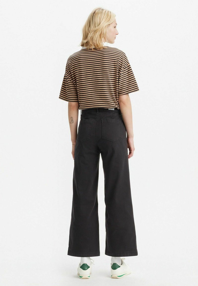 Maglietta cropped a strisce marrone e beige abbinata a pantaloni larghi neri a vita alta e scarpe da ginnastica con dettagli verdi.
