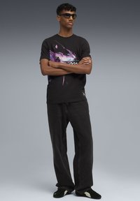 Camiseta de algodón negra con un gráfico de coche colorido, combinada con pantalones vaqueros negros y sueltos, y zapatos oscuros con detalles blancos.