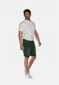 Un polo blanc à manches courtes et col, associé à un bermuda vert jusqu'aux genoux. Les baskets sont blanches avec des accents roses.