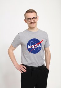 Grijze katoenen t-shirt met een blauw NASA-logo, witte tekst en rode accenten, gecombineerd met zwarte broeken.