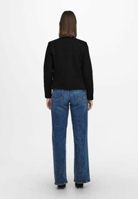 Svart figursydd jacka i texturert tyg, tillsammans med högmidjade blå jeans. Jeansen har en klassisk denimfinish och synliga bakfickor.