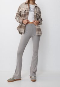 Plaid shirt in beige and brown over a white cropped top; light gray ribbed flared pants and gray sneakers with white laces and brown sole.