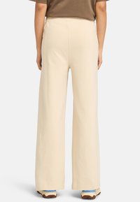 Crème-gekleurde wijde broek gemaakt van een zachte, lichtgewicht stof, met een elastische taille en die naar de onderkant toeloopt.