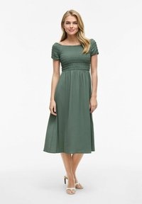 Grön midi-klänning med smockad bodice, korta puffärmar och en flödande kjol. Tillverkad av lättviktig tyg med subtil textur.