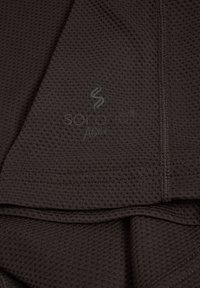 Tissu texturé gris foncé avec des coutures visibles et un logo subtil « Sorona® Active » imprimé sur le matériau.