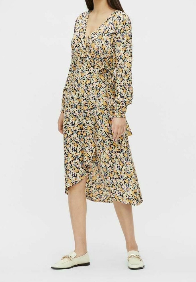 Kwiatowa sukienka midi z fasonem kopertowym, długimi rękawami, dekoltem w kształcie litery V, w żółte i fioletowe wzory, teksturowana tkanina i falbaniasty dół. W zestawie z białymi loafersami.
