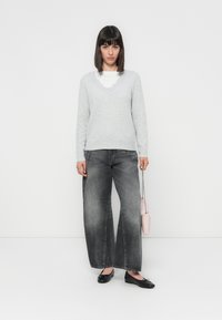 Lichtgrijze v-hals trui met golvende randen, gecombineerd met brede grijze jeans. Zwarte ballet flats en een kleine roze handtas maken de outfit compleet.
