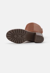 Brun mockask ankle boot med en strukturerad gummisula som har ett greppmönster och en måttlig klackhöjd. Designen inkluderar subtila sömdekorationer.