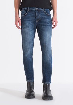 Vaqueros de mezclilla azul con un corte ajustado, que presentan un ligero desvanecimiento, cinco bolsillos y un diseño de pierna recta. Combinados con botas negras hasta el tobillo.