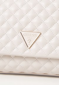 Bolso de mano de piel sintética gris acolchado con un acento de logo triangular dorado en la parte frontal y detalles de costura en contraste en todo el bolso.