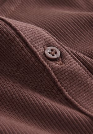 Primo piano di un tessuto marrone costellato, con un dettaglio di bottoni. La trama sembra morbida con cuciture visibili lungo i bordi.