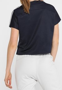 Maglietta atletica croppata di un blu navy scuro con maniche corte, caratterizzata da strisce laterali bianche e un tessuto morbido e leggero. Vista dal retro mostrata.