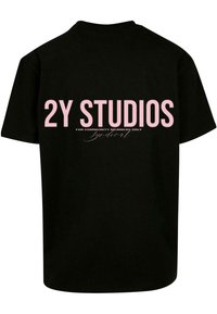 Čierne bavlnené tričko s ružovým textom na chrbte, ktorý znie "2Y STUDIOS IBA PRE ČLENOV KOMUNITY" s kurzívnym akcentom nižšie.