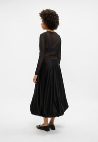 Fekete, hosszú ujjú hálós felső, amelyet egy lágy fekete selyemszerű szoknyával párosítottak, ballon formával, és lapos fekete cipővel, tüskés díszítéssel.