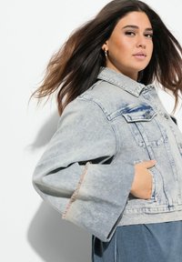 Ljusblå denimjacka med utsvängda ärmar och fransiga manschetter. Har klassisk krage, framfickor och lätt blekning för textur.